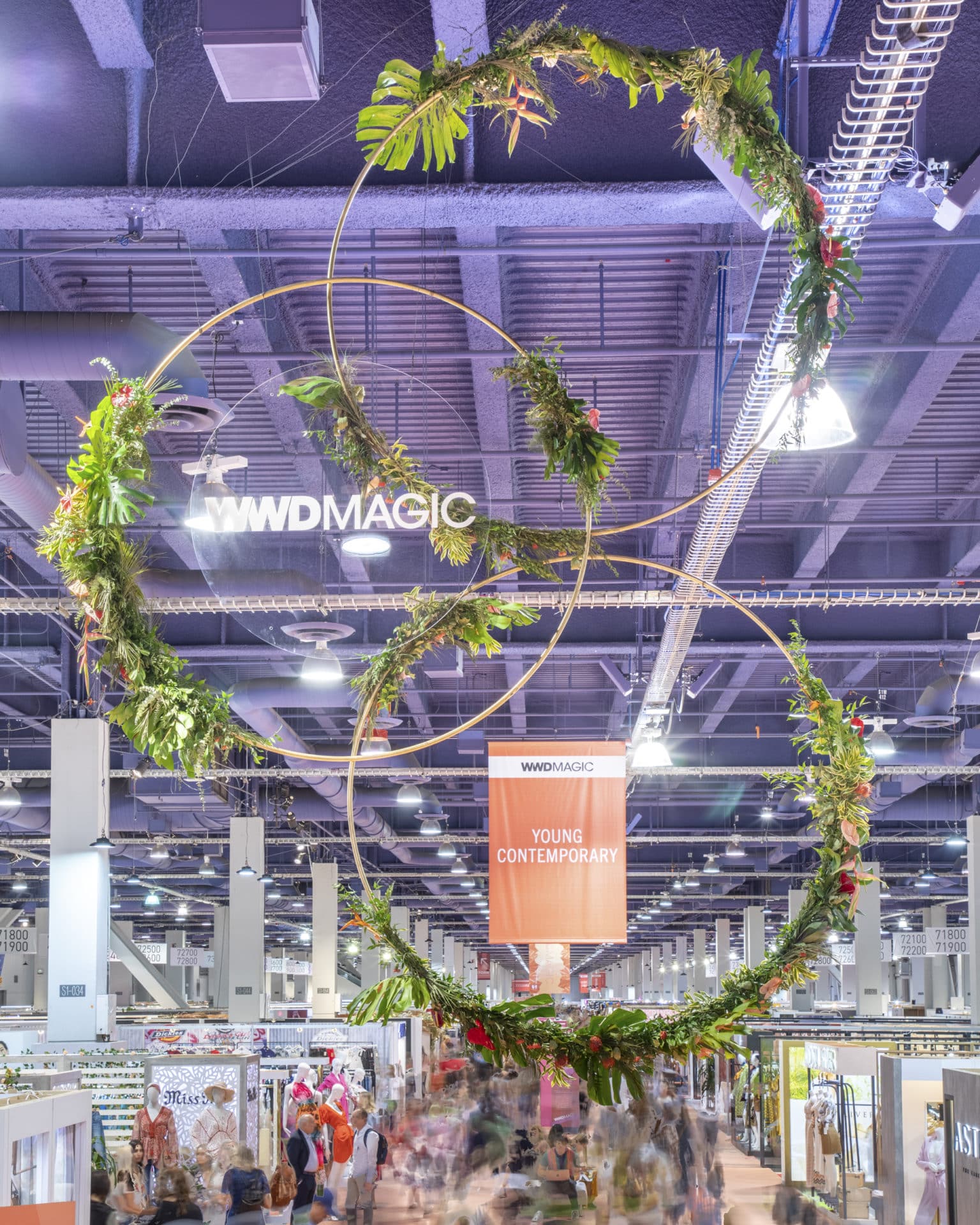 Plant rental display on circular structures hanging from the ceiling above a trade show floor.