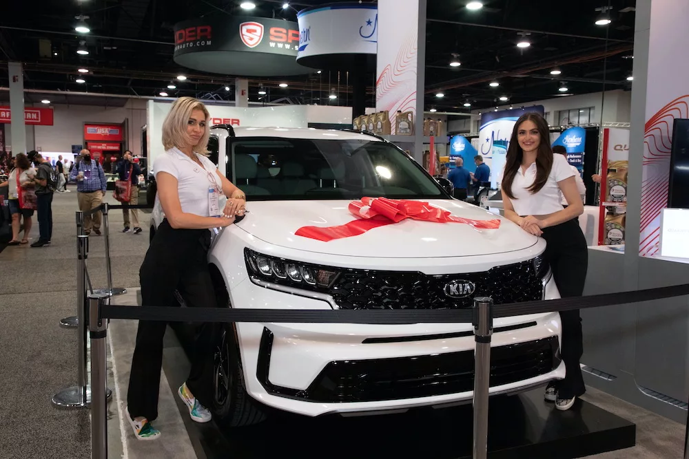 Trade show models standing next to a  white vehicle on display.