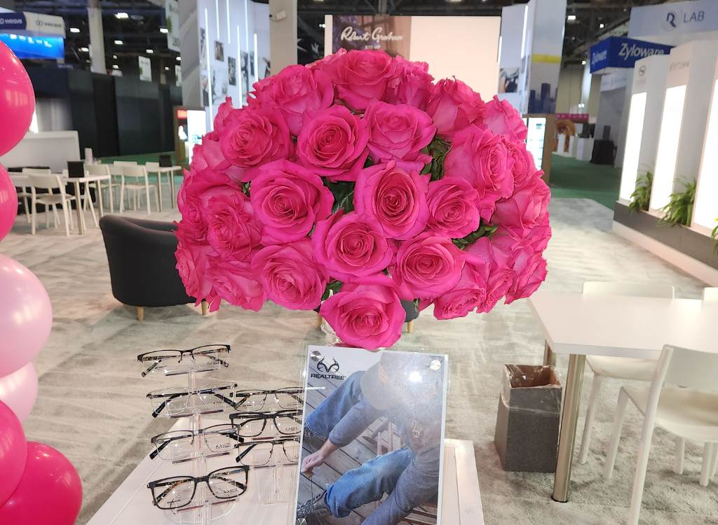 Large bouquet of pink flowers sitting on a table at an eye glasses trade show exhibit.