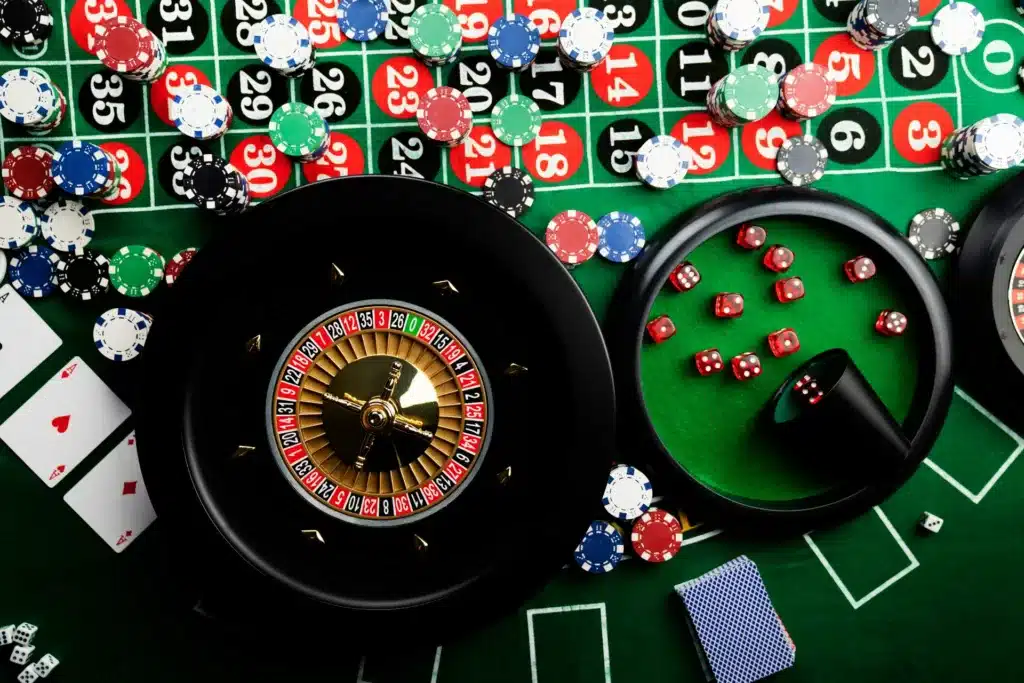Roulette wheel, cards, and poker chips on a green casino table.