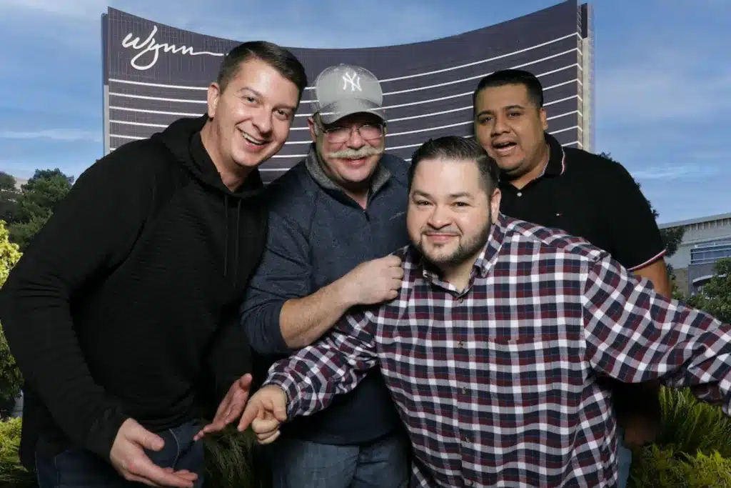 Group of four men posing in front of a green screen image of the Wynn in Las Vegas, Nevada.