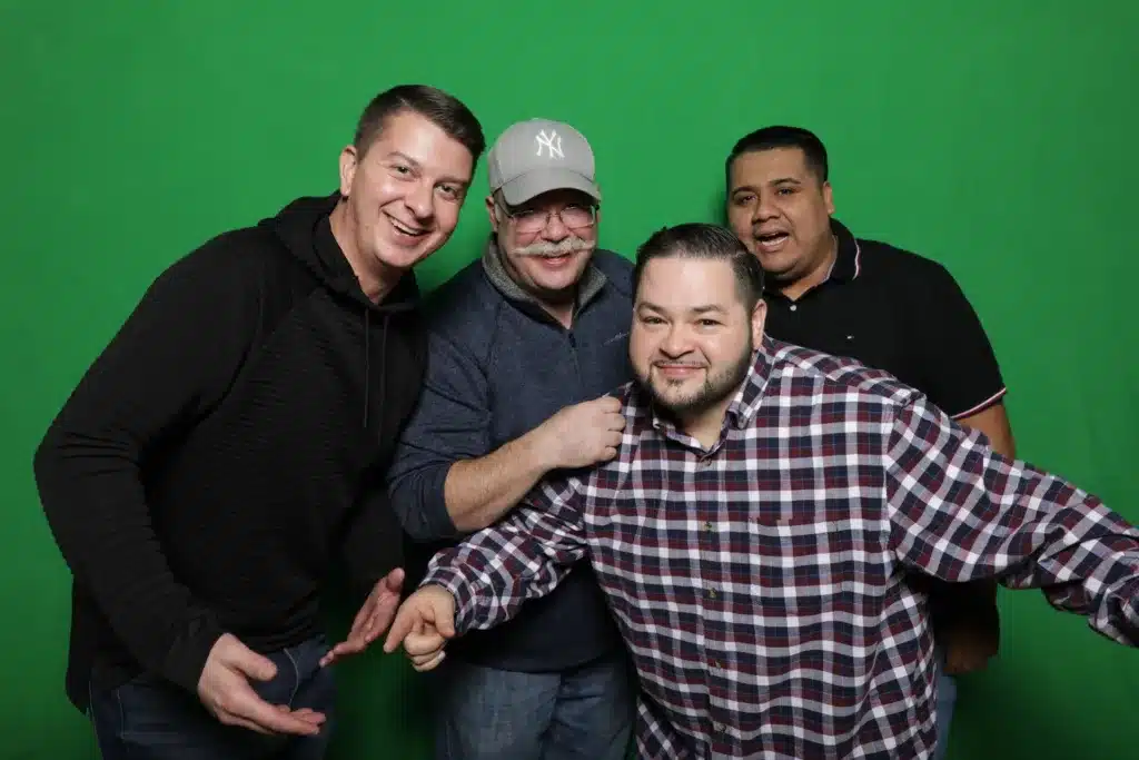 Group of four men posing in front of a green screen.