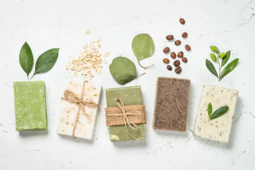Five bars of soap with natural ingredients like plants and coffee beans in the background.