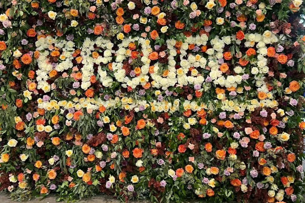 Word 'project' in white flowers surround by multi-colored flowers and plants on a wall.