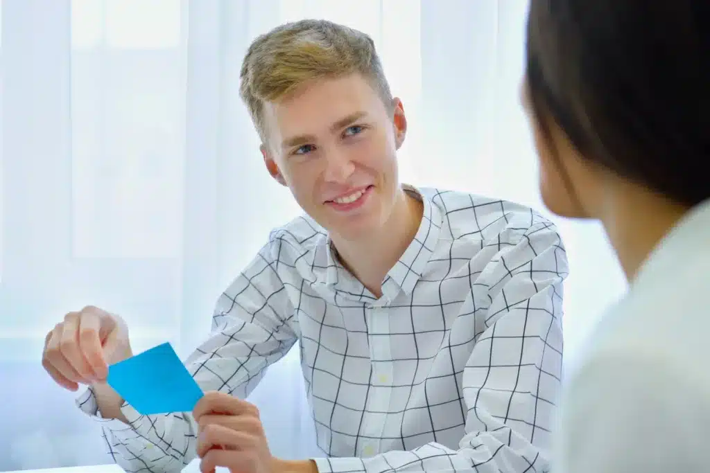 Young man holding a note card while talking to another person.