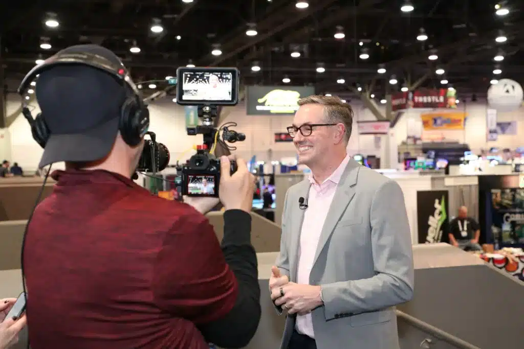 Man giving an interview in front of a video camera at a trade show. 