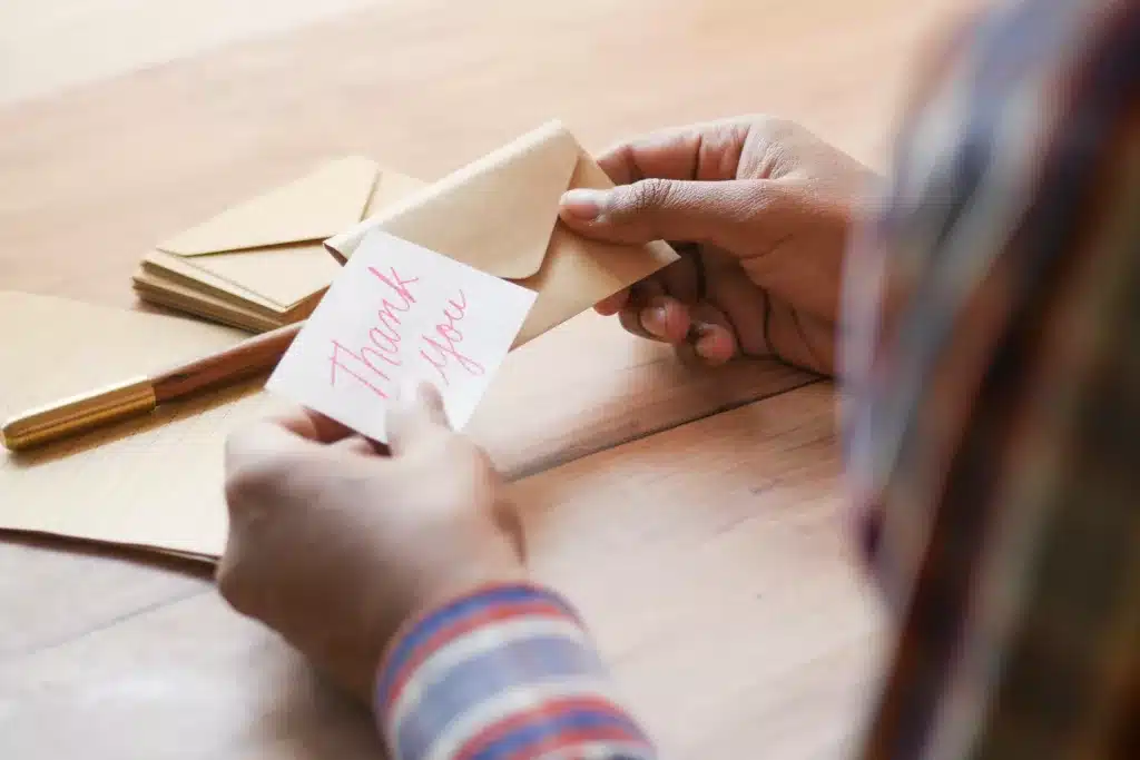 Pair of hands holding a notecard that has the text 'thank you' written on it in red pen.