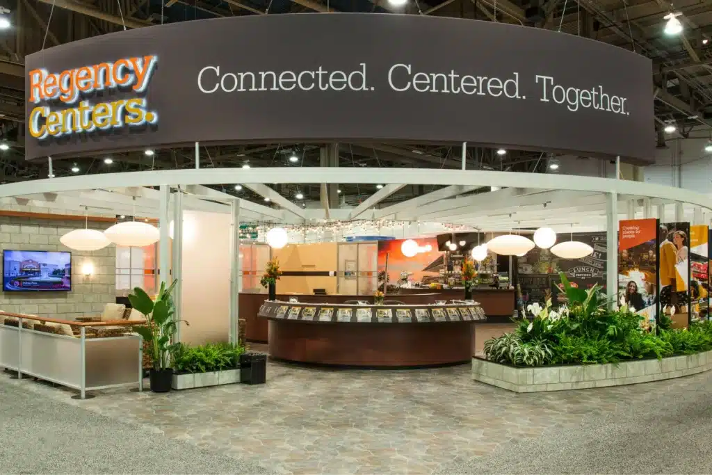 Trade show booth entrance with plants and signs.