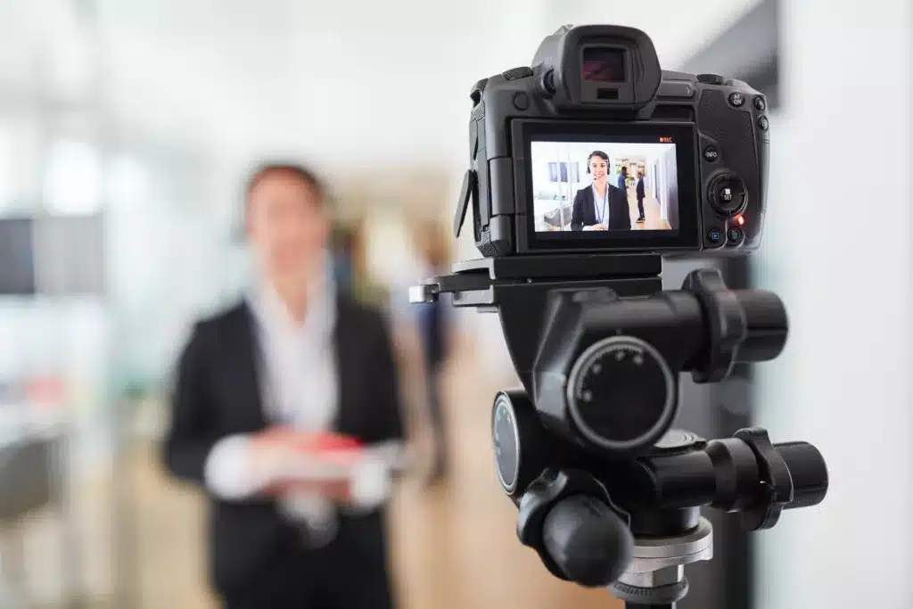 photo of a video camera filming a persona in the background.