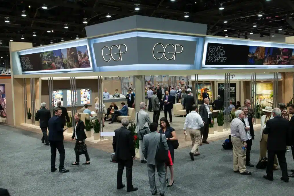 People walking and gathering at a booth at a large trade show conference center.