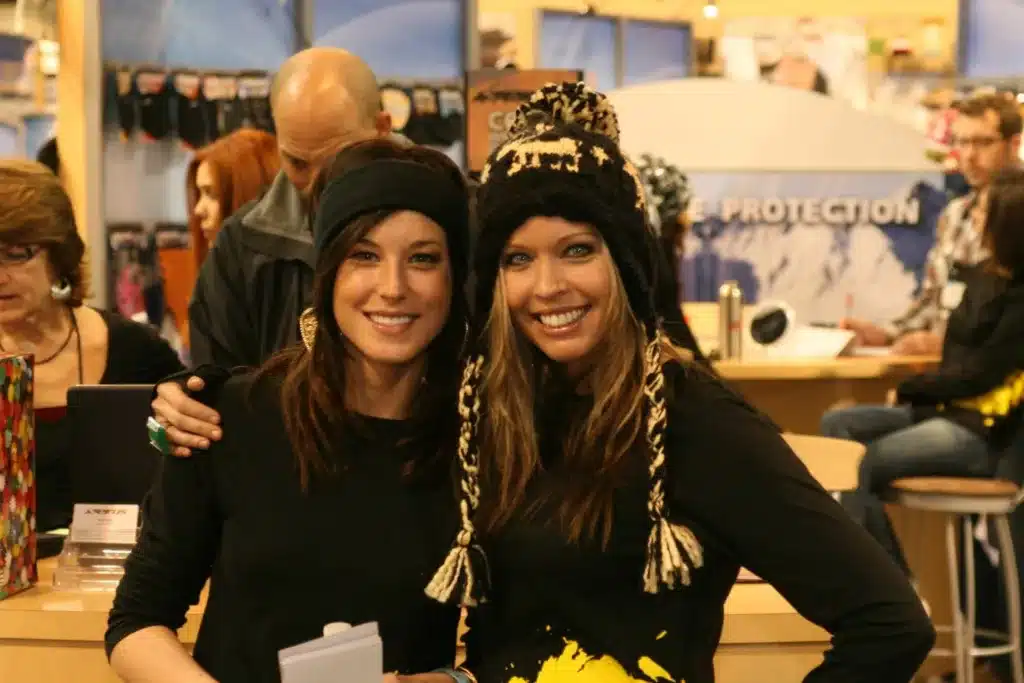 Two women in black shirts and black stocking hats at a trade show.