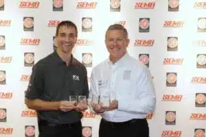 two men holding awards standing in front of a photo backdrop