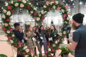 group of people posing for a photo next to a giant heart made of flowers and greenery