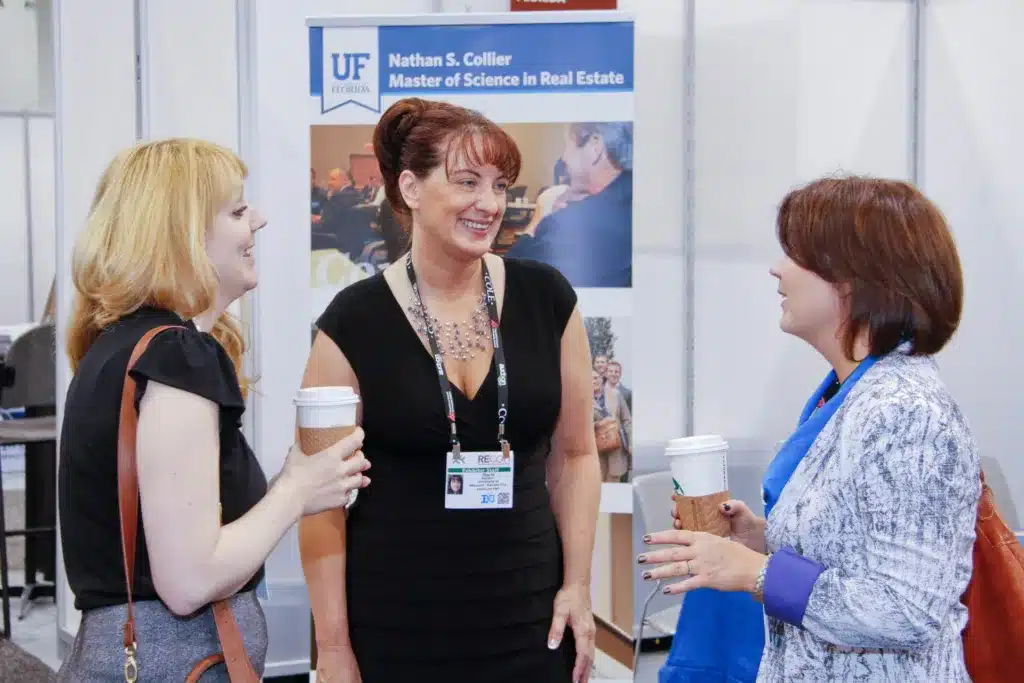 three women standing while talking, two with coffee cups in their hands